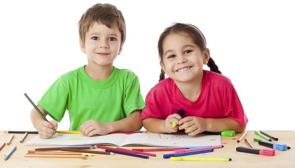 Two smiling little kids at the table draw with crayons, isolated on white